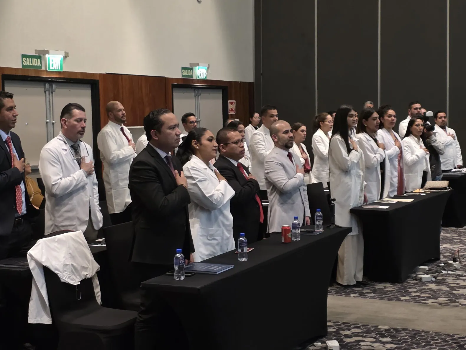 Ceremonia institucional de médicos del IMF con bata blanca entonando el himno nacional